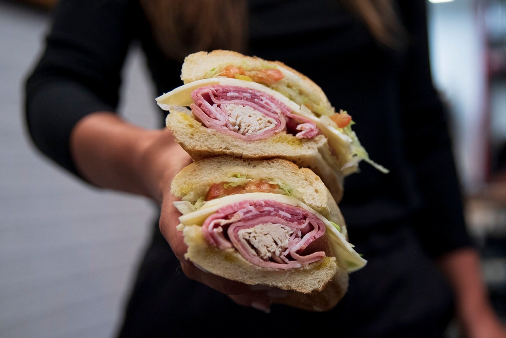 A sandwich with meats and cheese cut in half and stacked one half on the other.