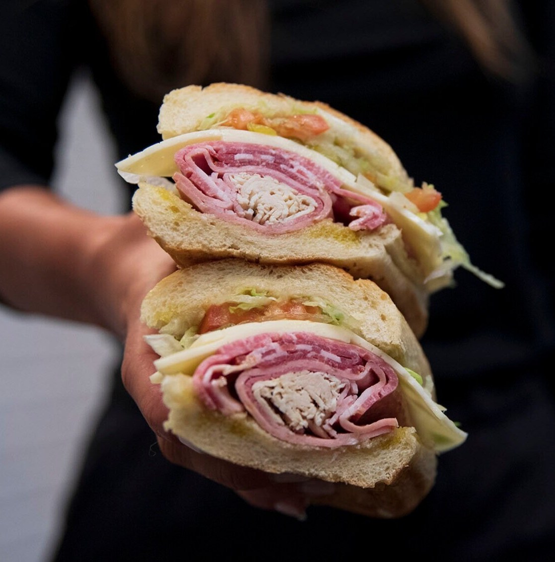 A sandwich with meats and cheese cut in half and stacked one half on the other.