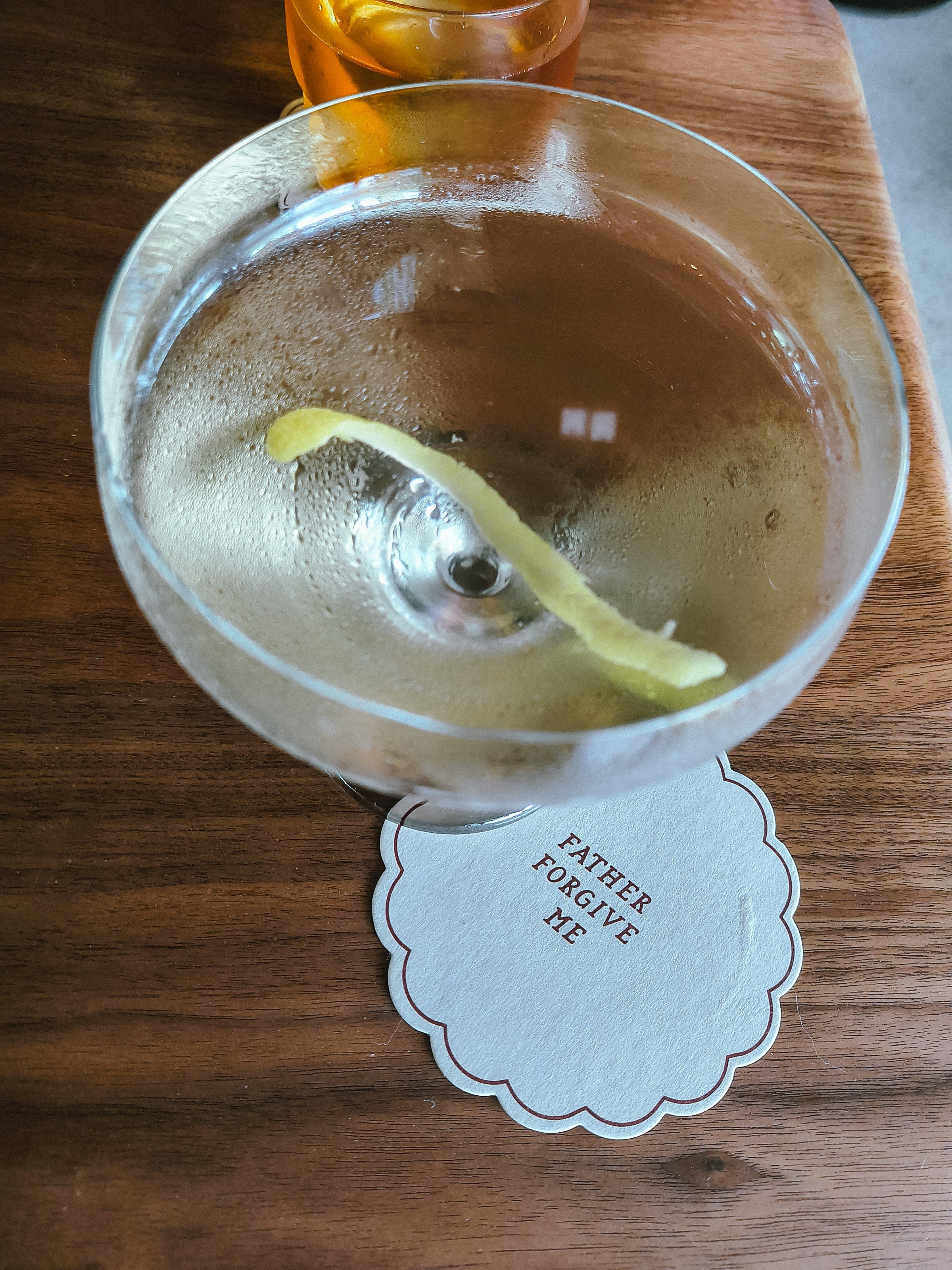 A cocktail on a coaster that says Father Forgive Me.