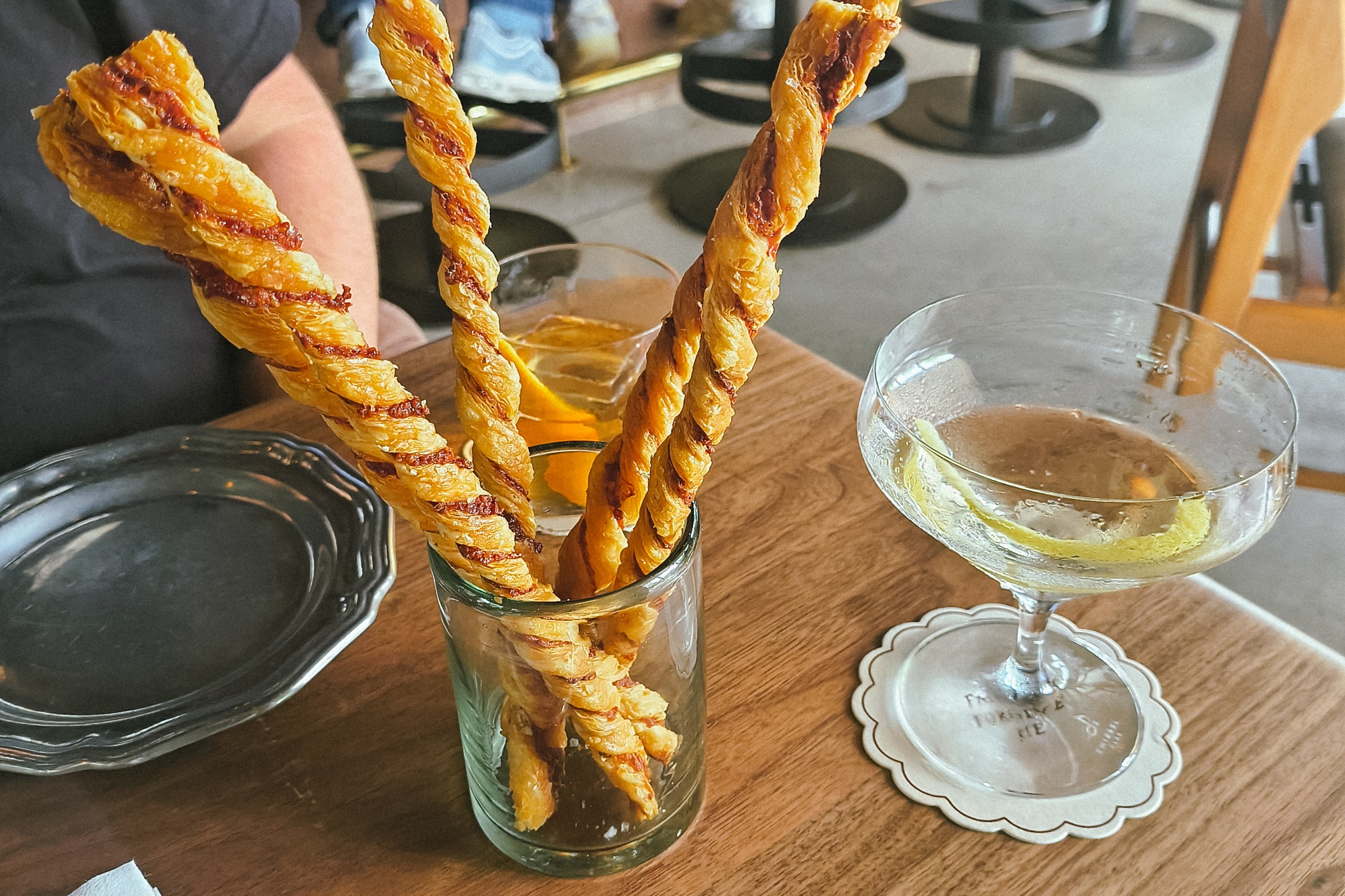 Sacristan stand upright in a glass next to a cocktail in a coup. 