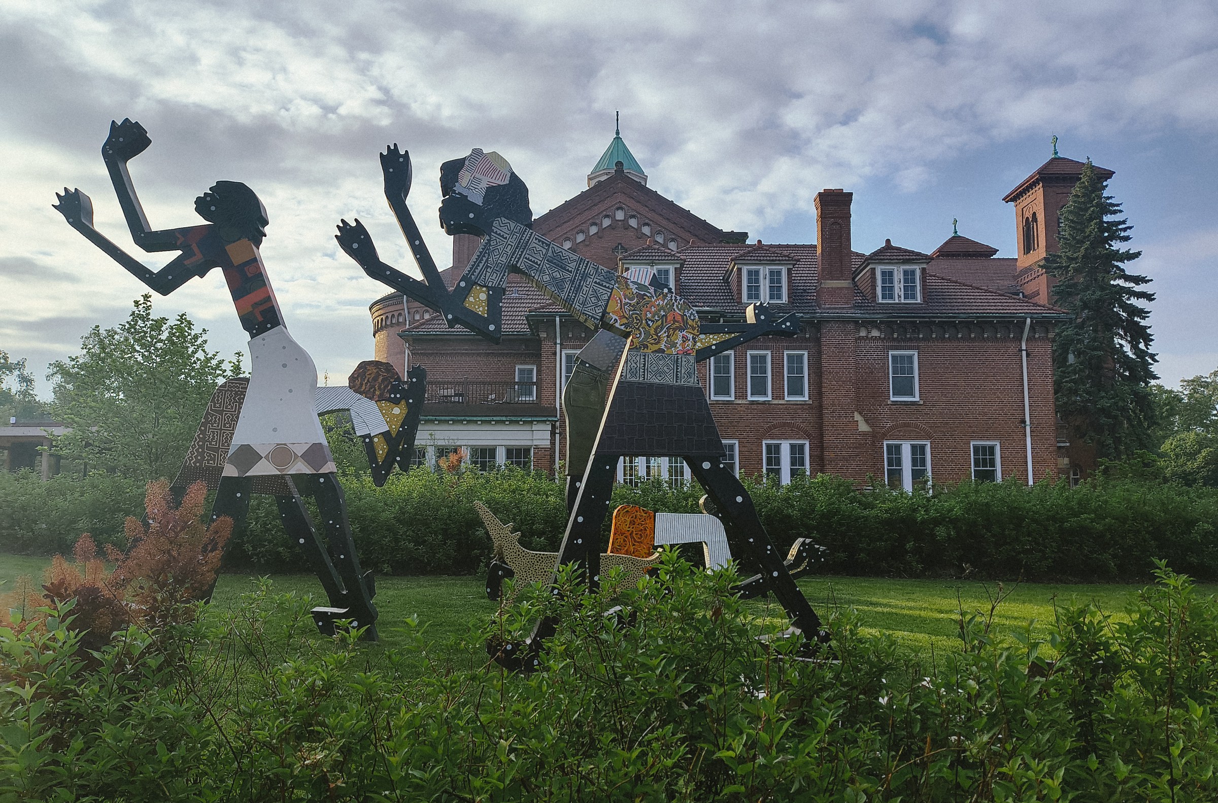 A view of a Romanesque church behind Black statue art installed on the lawn. 