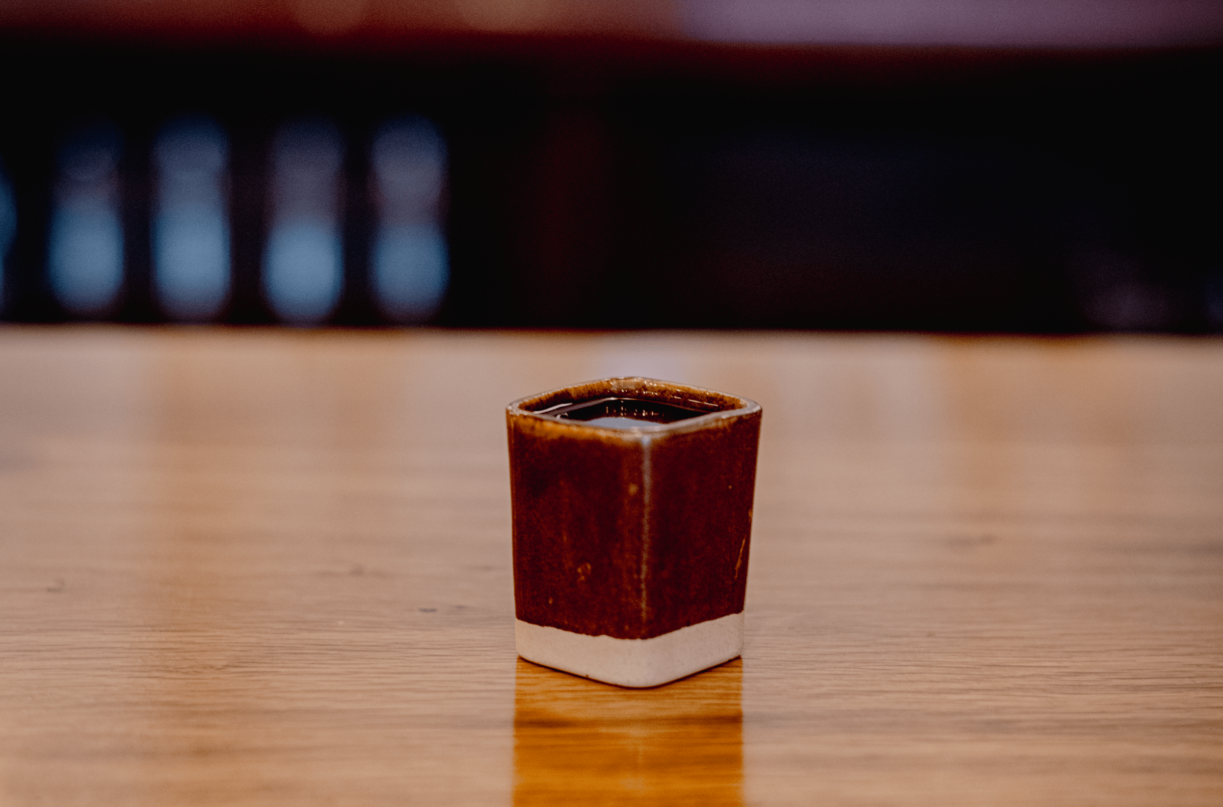 A square, brown, ceramic shot glass. 